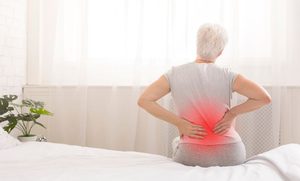 Sore senior woman sitting up in bed 