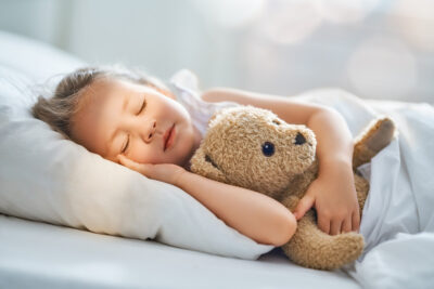 Child sleeping while hugging teddy bear.