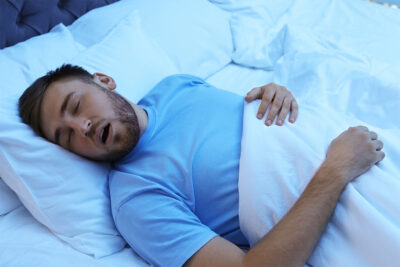 A man in bed, mouth open while sleeping, depicting a common symptom of sleep apnea.